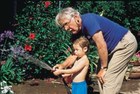Grandfather and grandson watering a garden with a garden hose.